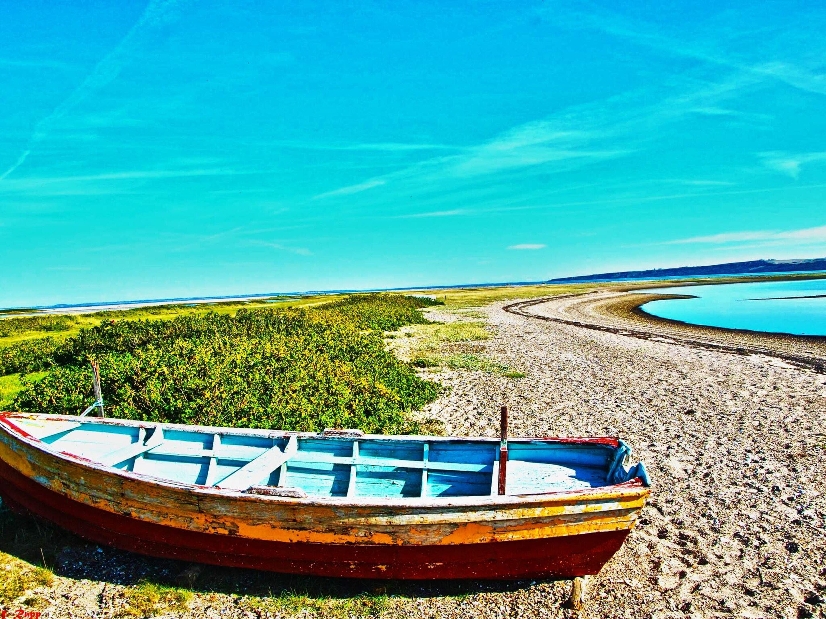 A boat on a pebbly shore with a lake and greenery in the background.