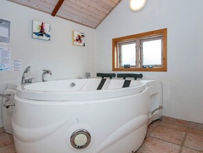 A bathroom with a large bathtub, a window, and two wall-mounted artworks.