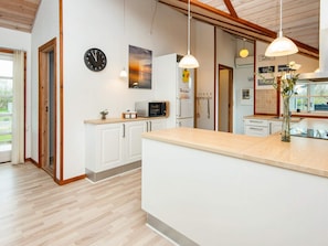 A modern kitchen with white cabinets, a wooden countertop, a clock, pendant lights, and a view of the outdoors.