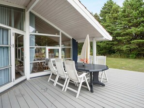 A covered outdoor deck with a table and chairs, large windows, and a view of the surrounding greenery. - 4 Star Holiday Home in Rodby (Rodby)