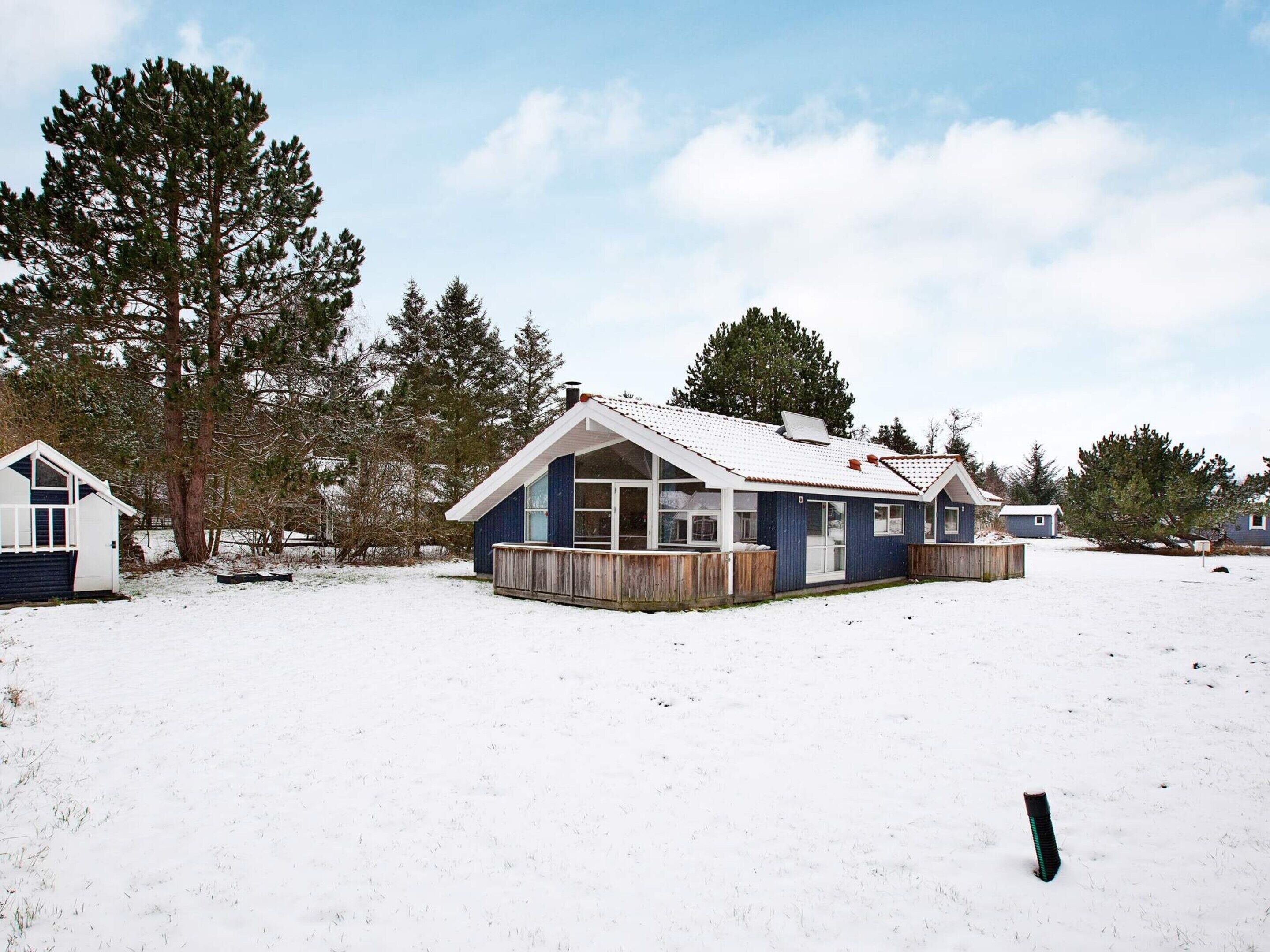 Ein eingeschossiges Haus mit Satteldach, umgeben von verschneitem Gelände und hohen Bäumen.