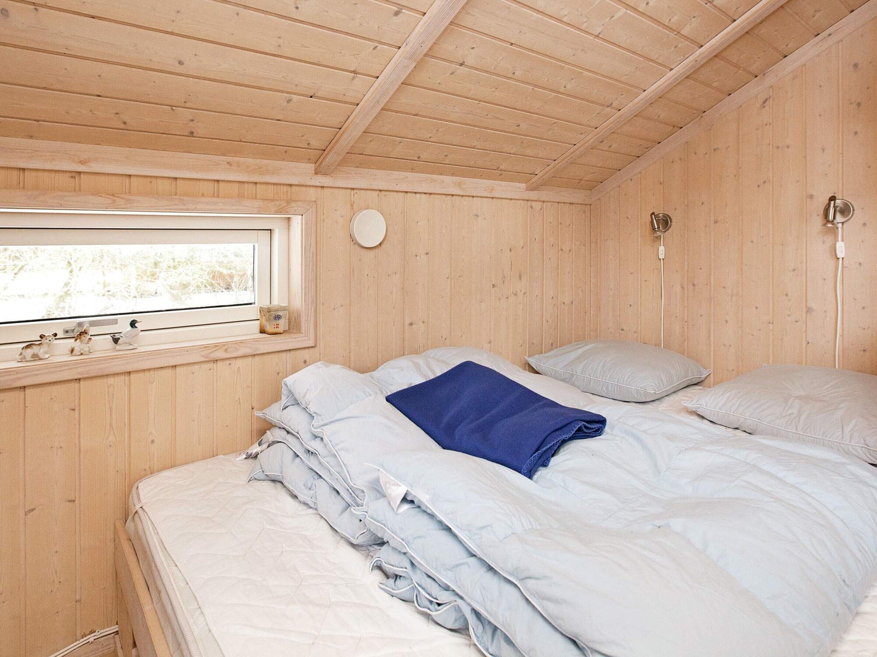 Ein Zimmer mit Holzwandverkleidung, einem Bett, einem Fenster und einer Wandleuchte.