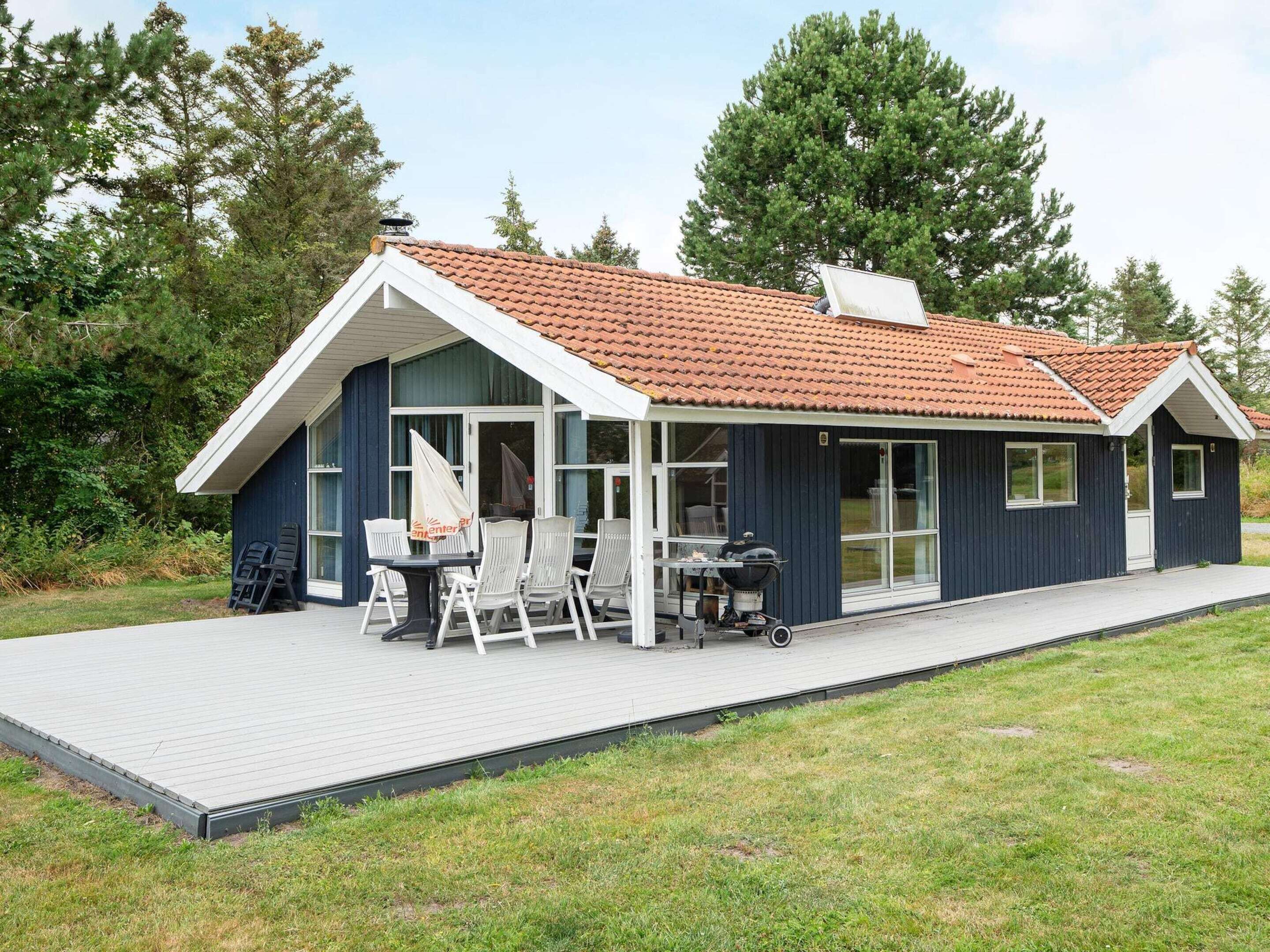 A modern house with a covered patio, a barbecue grill, and a dining area with chairs.