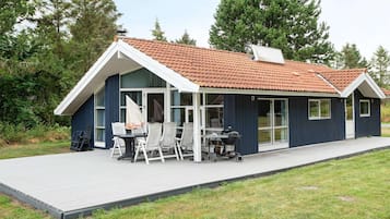 Una casa moderna con un porche cubierto, una parrilla para barbacoa y un comedor con sillas.