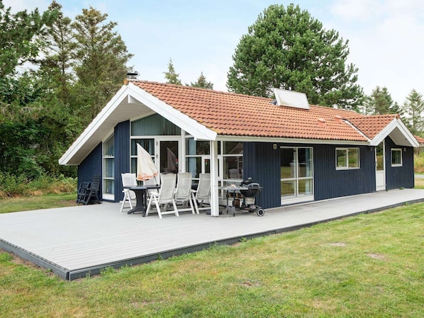 A modern house with a covered patio, a barbecue grill, and a dining area with chairs.