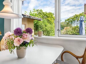 A dining area with a table, chairs, a vase of flowers, a window with a view of greenery, and a hanging light fixture. - Spacious Holiday Home in Allinge Bornholm near Sea (Allinge)