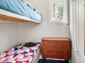 Un dormitorio con una cama litera, una cama individual, un aparador de madera y una ventana con vista a árboles.
