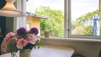 Una mesa con un florero, una ventana con vistas a follaje, y una lámpara.
