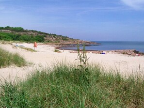 A beach with sand, grass, and a rocky shoreline.