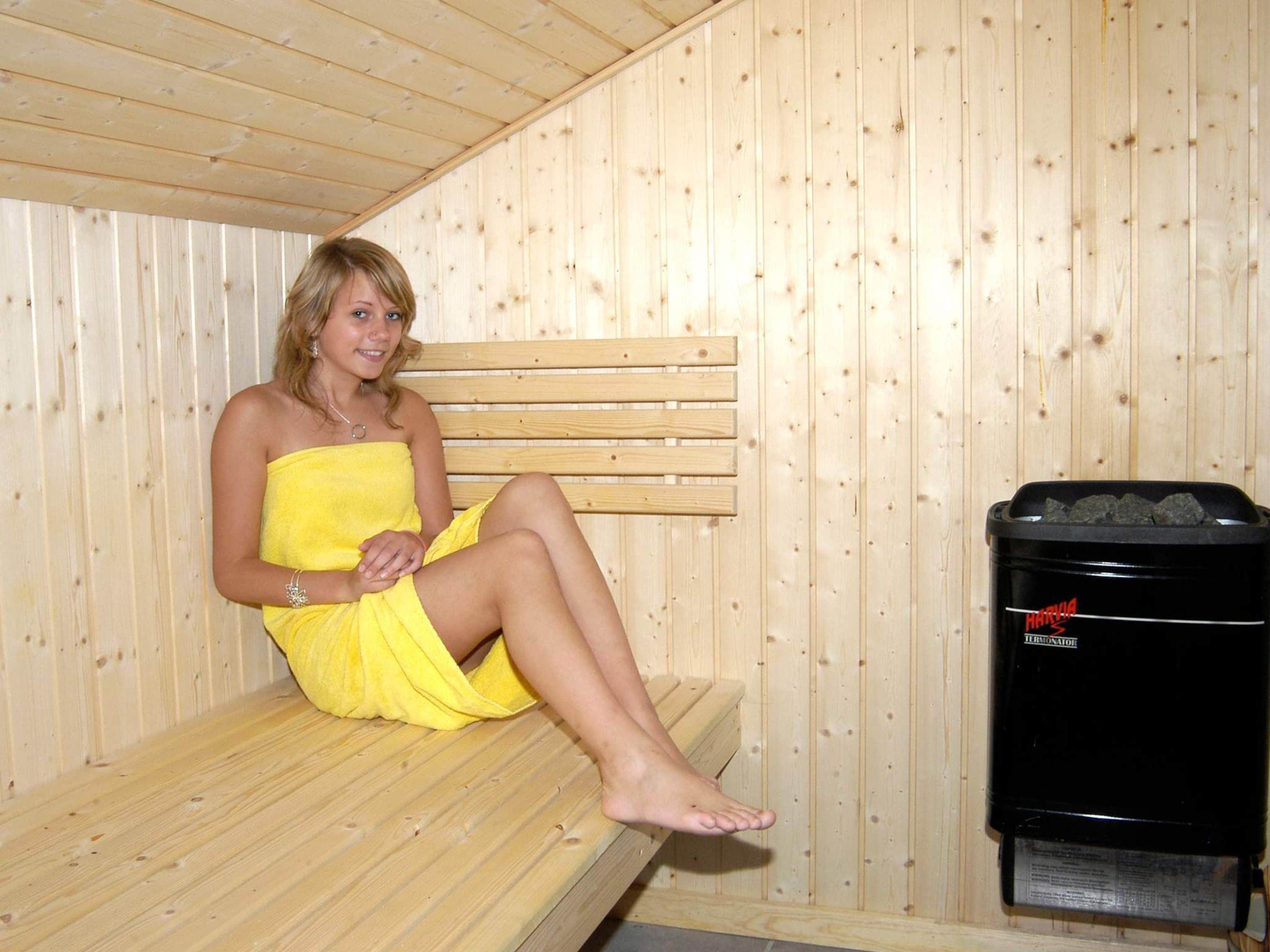 A person sitting on a bench in a wooden room with a sauna.