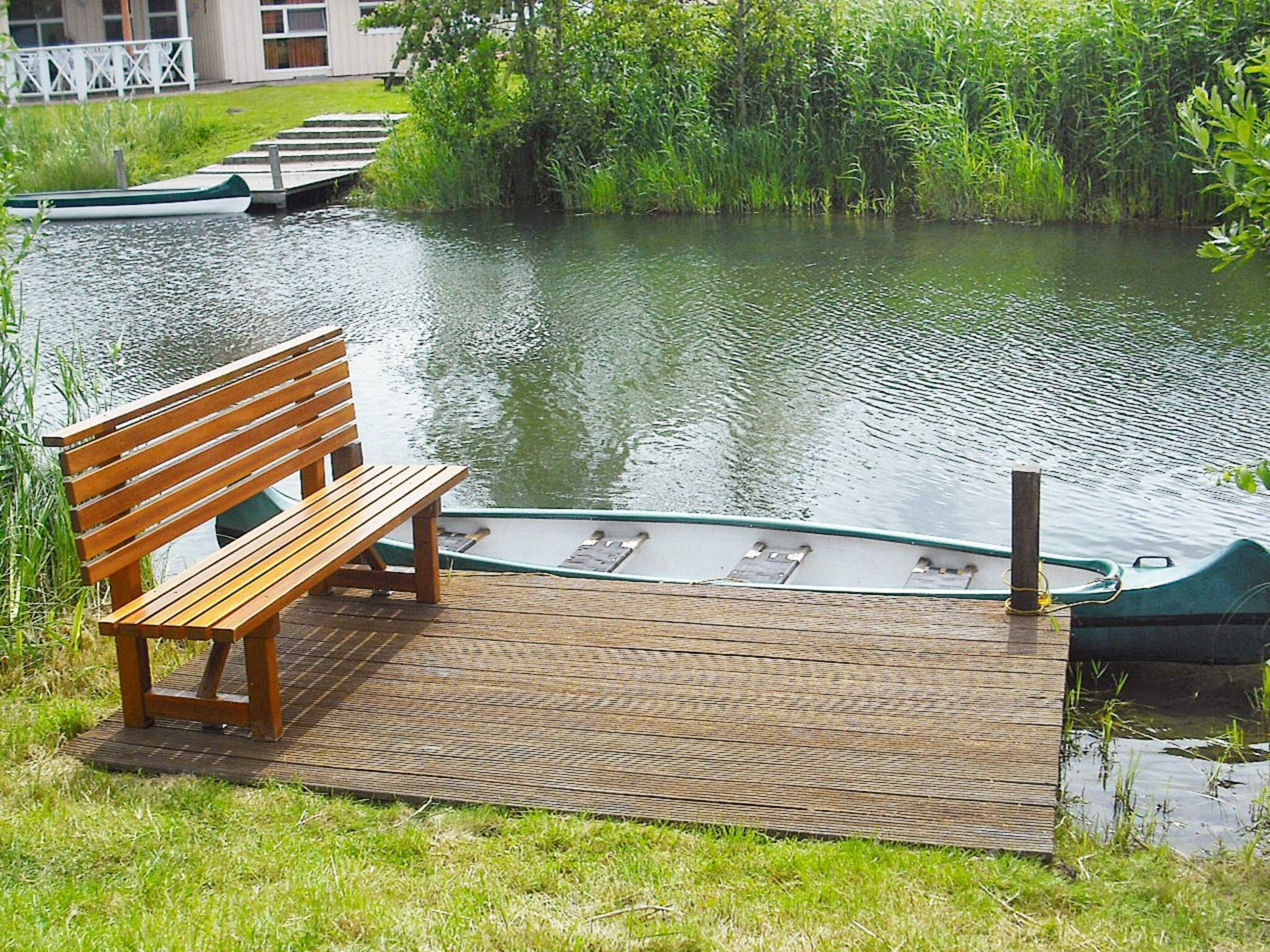 A wooden bench on a dock by a calm river with boats.