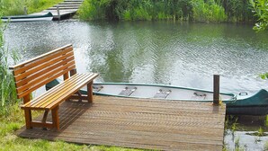 A wooden bench on a dock by a calm river with boats. - Holiday Home in Otterndorf (Otterndorf)