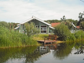 A house with a dock extending into a calm body of water, surrounded by lush greenery.