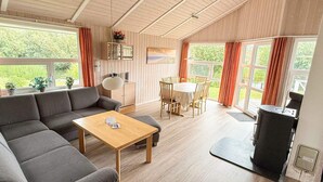 A modern living room with a sofa, a coffee table, a dining table with chairs, and a grill station. - Holiday Home in Otterndorf (Otterndorf)