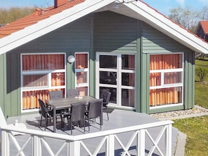 A covered outdoor area with a table and chairs, large windows with curtains, and a white railing. - Holiday Home in Otterndorf (Otterndorf)