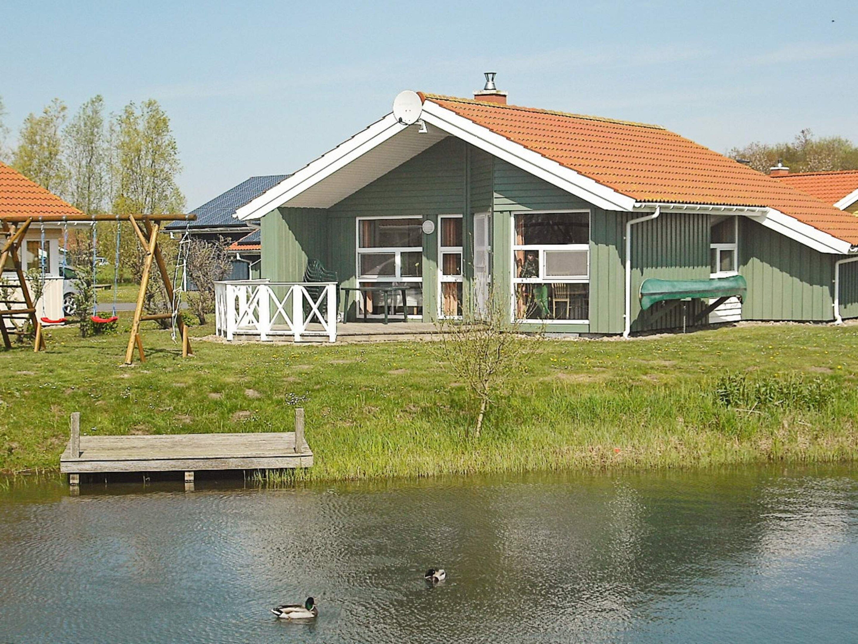 A green house with a sloped roof, a dock, and a pond with ducks.