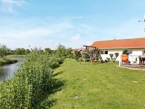 A house with a red-tiled roof, a wooden swing set, and a river in the background. - Holiday Home in Otterndorf (Otterndorf)
