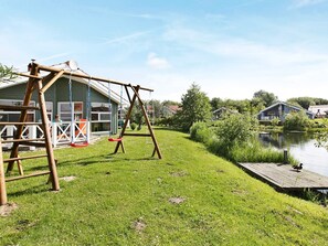 Een gazon met een houten schommel, een aanlegsteiger en een wateroppervlak.