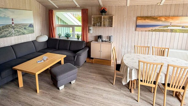 A cozy room with a sofa, a wooden table, a dining table with chairs, a cabinet, and a window with curtains. - Holiday Home in Otterndorf (Otterndorf)