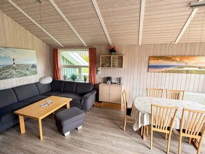 A cozy room with a sofa, a wooden table, a dining table with chairs, and a cabinet. - Holiday Home in Otterndorf (Otterndorf)