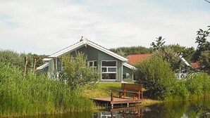 A house with a dock extending into a calm body of water, surrounded by lush greenery. - Holiday Home in Otterndorf (Otterndorf)