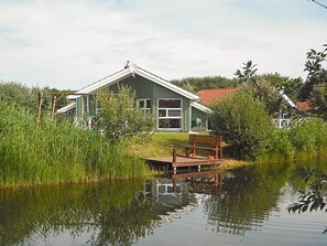 A house with a dock extending into a calm body of water, surrounded by lush greenery. - Holiday Home in Otterndorf (Otterndorf)