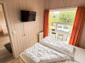 A room with a bed, a television mounted on the wall, and a window with curtains. - Holiday Home in Otterndorf (Otterndorf)