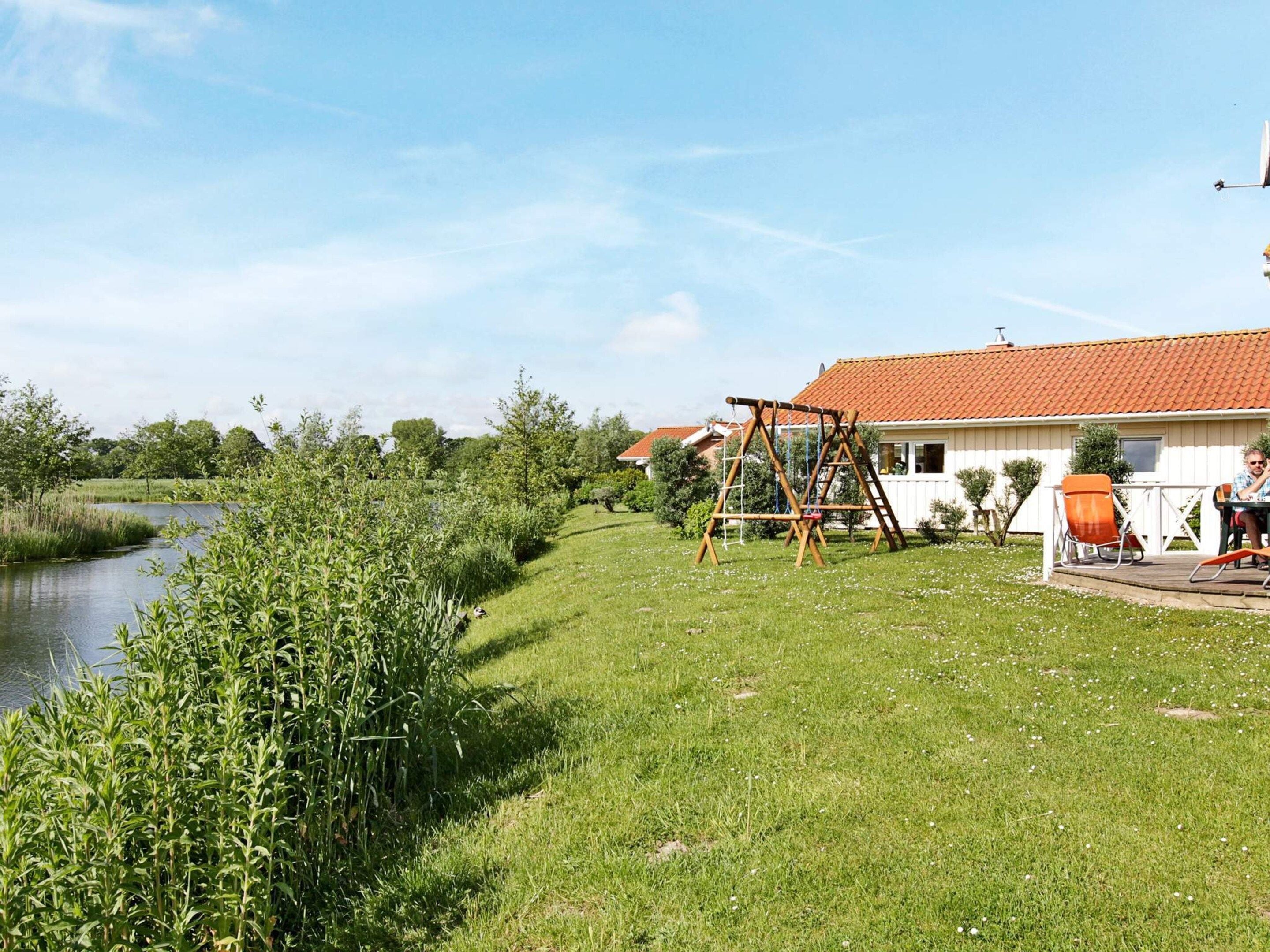 Ein Wohnhaus mit Rasen, einer Holz-Schaukel, einem kleinen Teich und einem Dach mit roten Ziegeln.