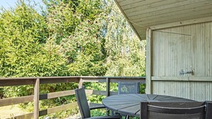 An outdoor deck with a round table and chairs, surrounded by a wooden railing and dense greenery. - 6 Person Holiday Home in Glesborg (Glesborg)
