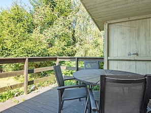An outdoor deck with a round table and chairs, surrounded by a wooden railing and dense greenery.