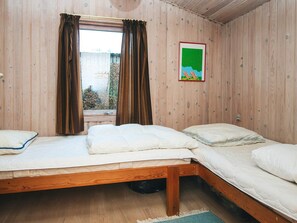 Ein Zimmer mit zwei Holzbettställen, einem Fenster mit Vorhängen und einem gerahmten Bild an der Wand.
