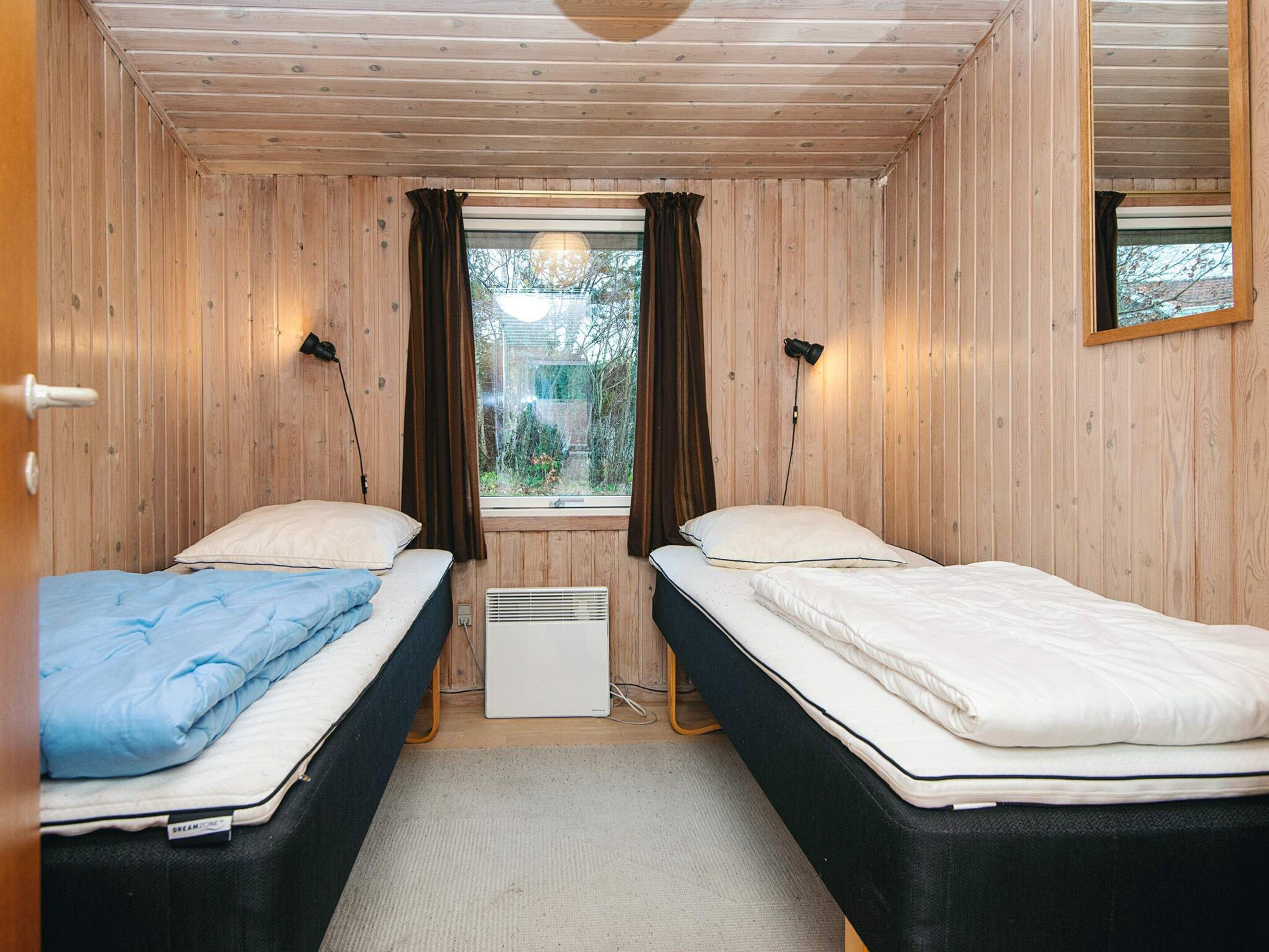 Eine Holzhütte mit zwei Betten, Vorhängen am Fenster und einer Heizung.
