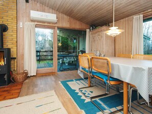 A cozy room with a fireplace, wooden walls, a dining table with chairs, and a view through a glass door.