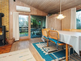 Una habitación acogedora con chimenea, paredes de madera, una mesa de comedor con sillas y vistas a través de un ventanal.