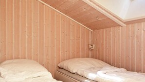 Quarto com duas camas, paredes de madeira e teto inclinado.