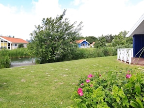 A grassy area with a pond, a blue house with a white fence, and a white structure with a blue roof. - Holiday Home in Otterndorf (Otterndorf)