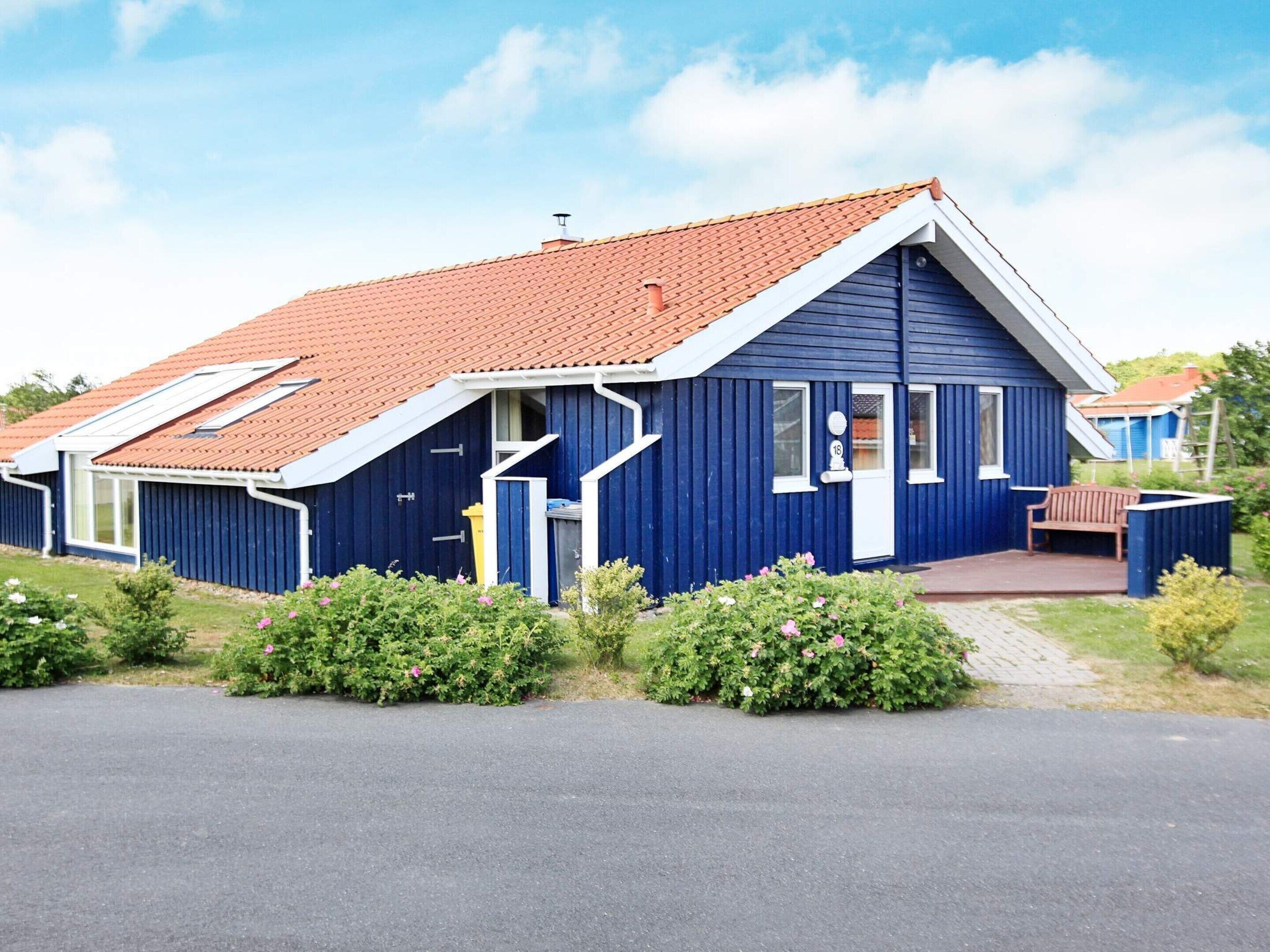 A blue building with a red roof, a front porch, and a small garden area.