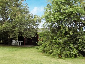 A grassy outdoor area with a white table and chairs, surrounded by trees and a building with a red roof.