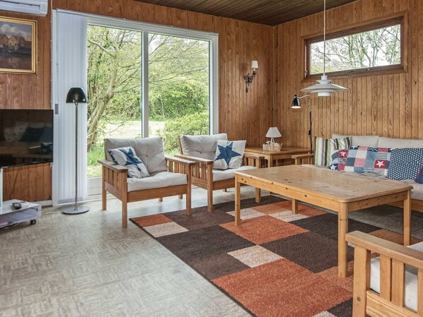 A cozy room with a wooden interior, a sofa, two chairs, a table, and a television.