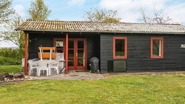 En lille, sort bygning med tegltag, en træbænk og et overdækket udendørs siddeområde.