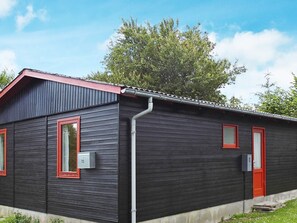 A small, single-story building with a dark exterior and red-framed windows, a red door, and a visible number '13' on the side.