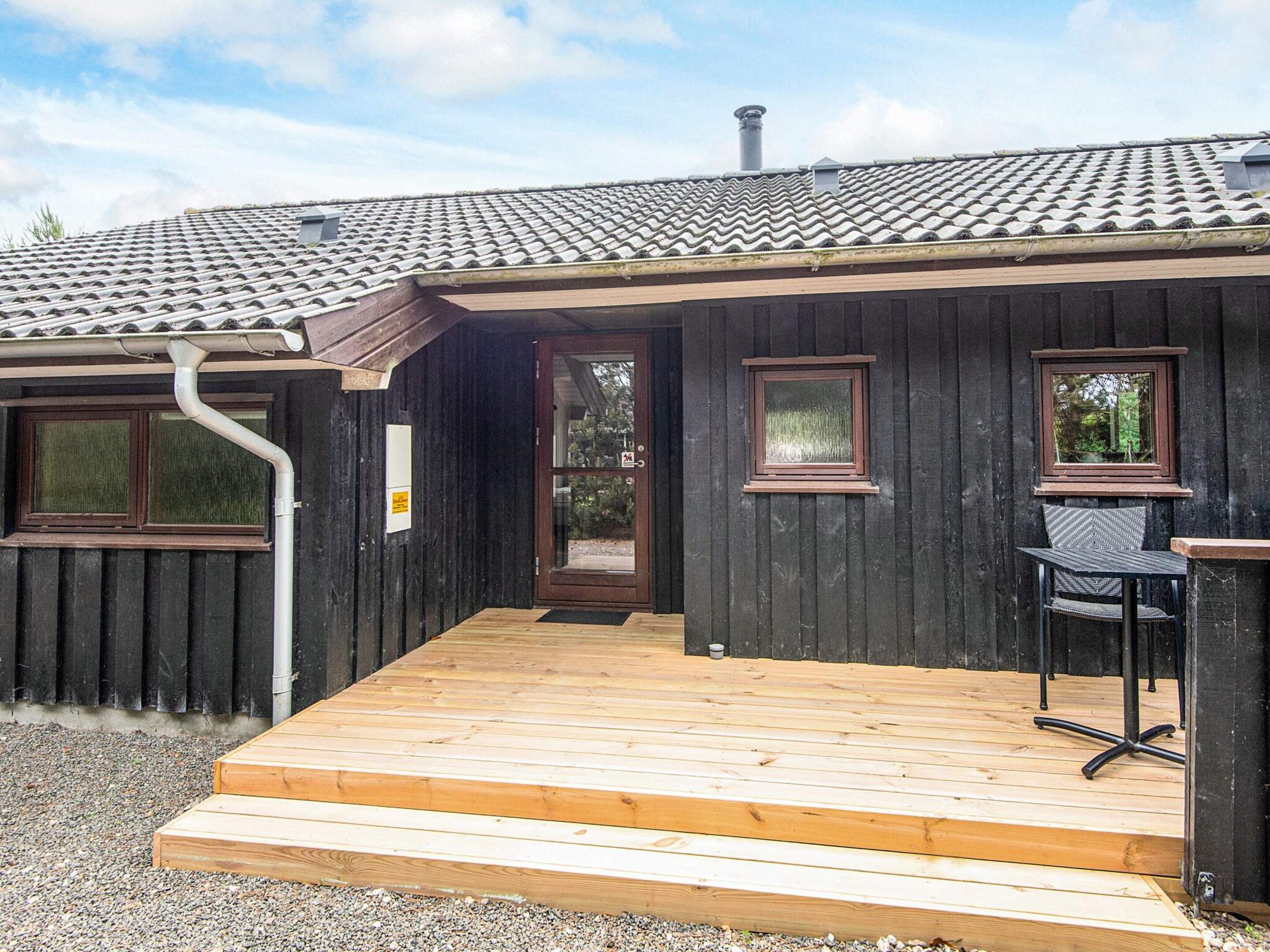 En träbyggnad med ett tak täckt av tegelpannor, en träveranda och en dörr med ett fönster.