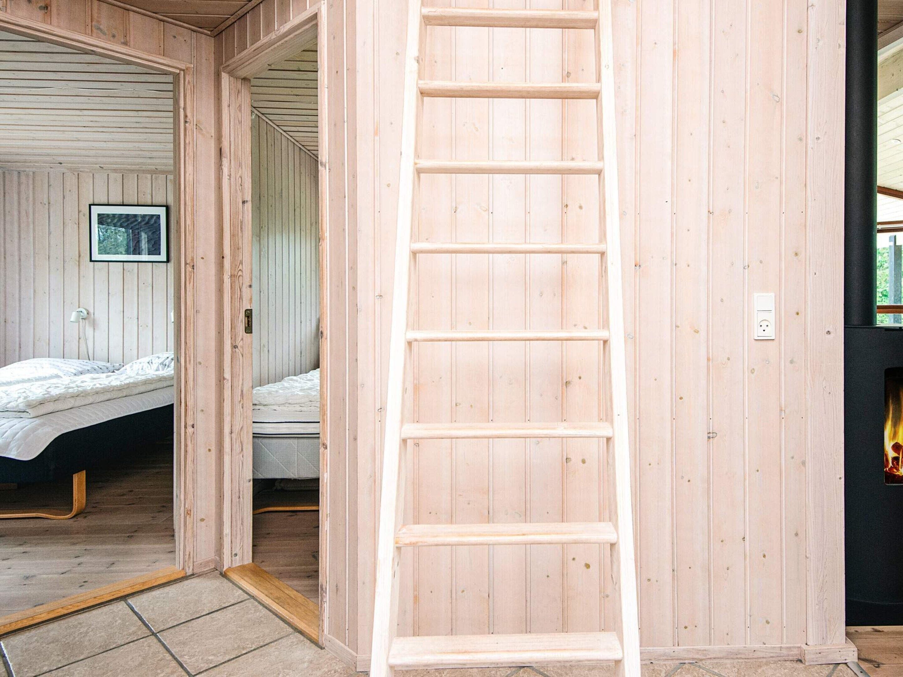 Un intérieur en bois avec une échelle, un lit et un tableau encadré au mur.