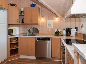 Cocina compacta con armarios de madera, lavavajillas, microondas y cafetera.