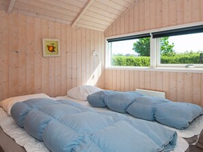 Una habitación con paredes de madera, una cama con ropa de cama azul, una ventana con vista a la vegetación y un cuadro enmarcado en la pared.