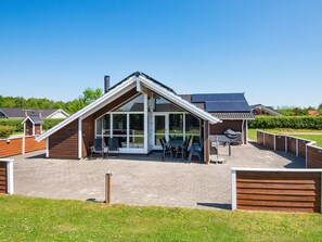 Una casa moderna con un amplio ventanal, un porche cubierto con muebles exteriores y un camino de ladrillo que conduce a la entrada.