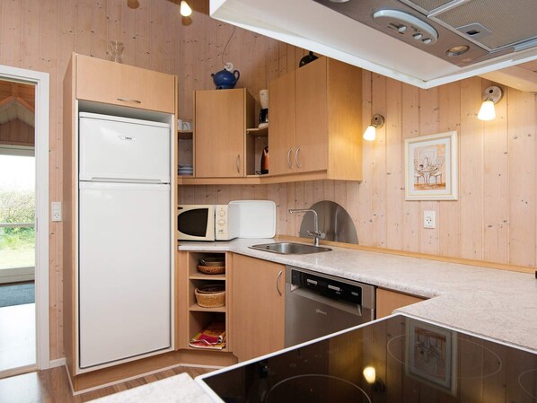 A compact kitchen with wooden cabinets, a white refrigerator, a microwave, a sink, and a dishwasher.