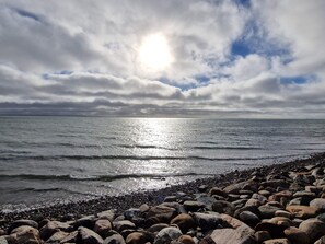 A rocky shoreline with waves, a cloudy sky, and a sun shining through.