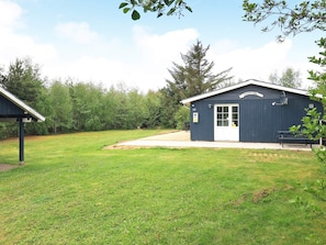 A small, single-story building with a white door and windows, surrounded by a grassy area and trees. - 4 Star Holiday Home in Thyholm (Thyholm)