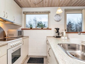 A compact kitchen with a microwave, stove, sink, and a clock on the wall. - 4 Star Holiday Home in Thyholm (Thyholm)